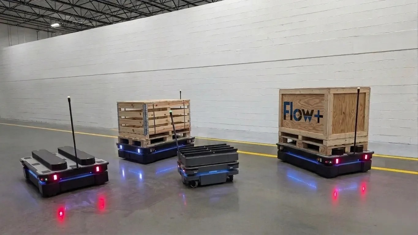 Three autonomous mobile robots in a warehouse, two carrying wooden crates on pallets
